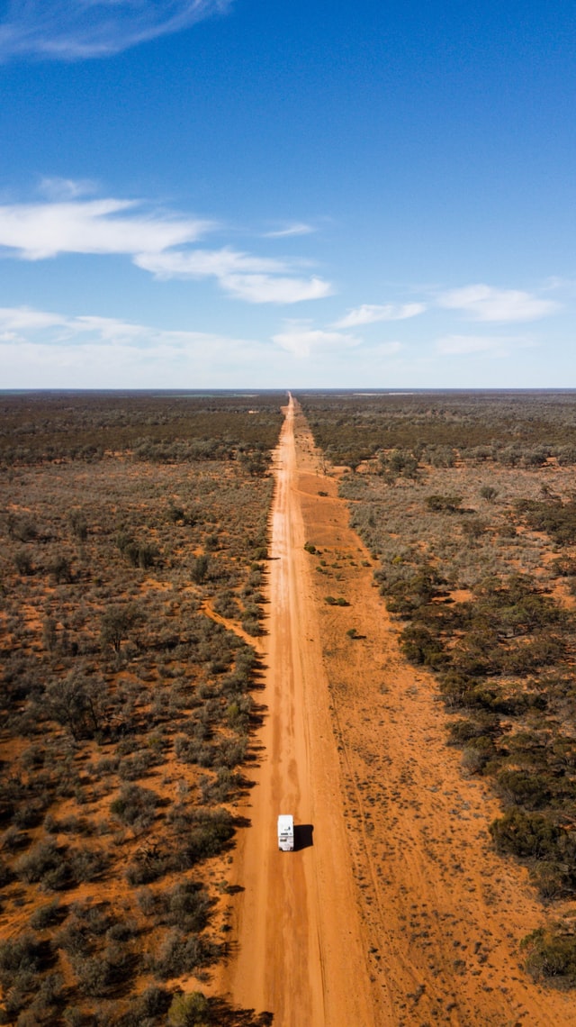 brown dirt road between green grass field under blue sky during daytime